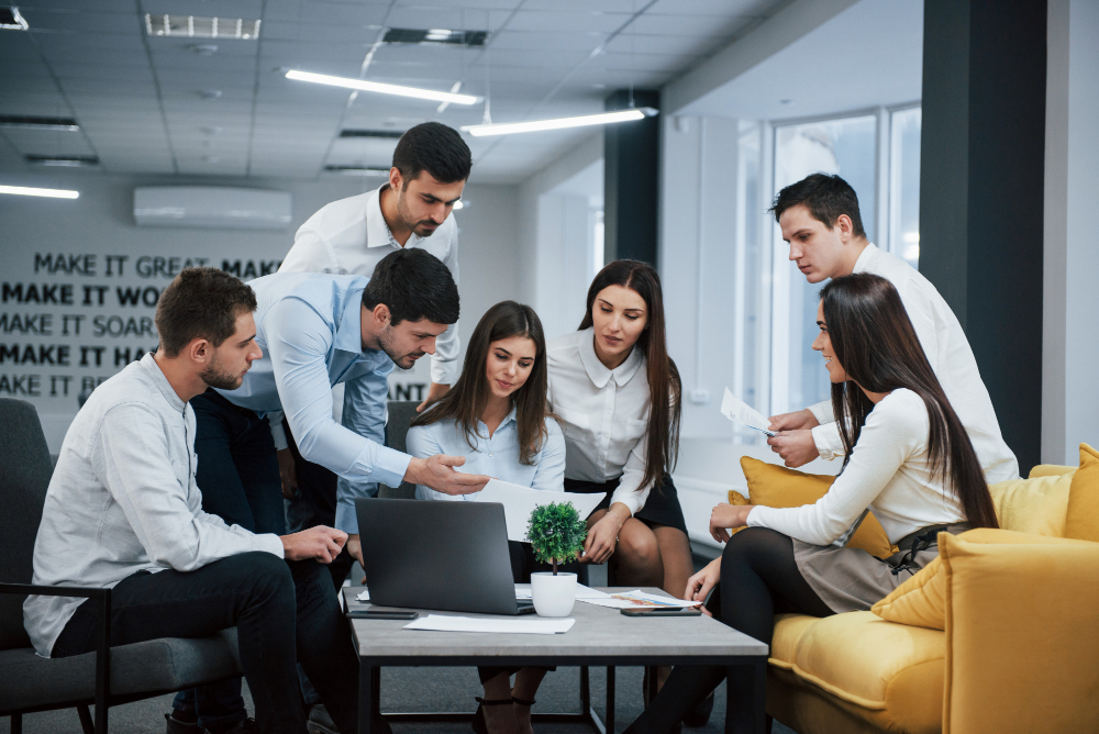 Guy shows document to a girl. Group of young freelancers in the office have conversation and working Guy shows document to a girl. Group of young freelancers in the office have conversation and working
